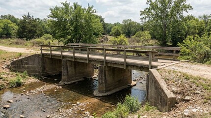 Fototapeta premium A small concrete bridge with wooden railings spans a shallow stream in a rural landscape