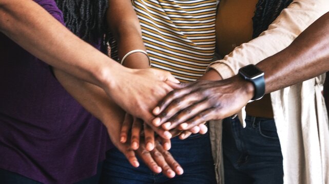 Diverse group of hands stacked together, symbolizing unity and teamwork. Hands of different ethnicities showing support and collaboration in a team effort. People stacking hands, unity and teamwork.