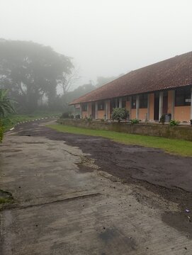 The image shows the building of SMK Negeri 1 Kuningan, located in the Kuningan area. The surrounding area appears foggy and surrounded by shady trees.