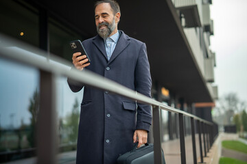 Executive man smiling holding briefcase using smartphone