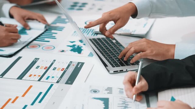 A dynamic business team collaborates to analyze financial data on digital devices, surrounded by detailed charts and graphs, showcasing modern office efficiency and teamwork. SACTR