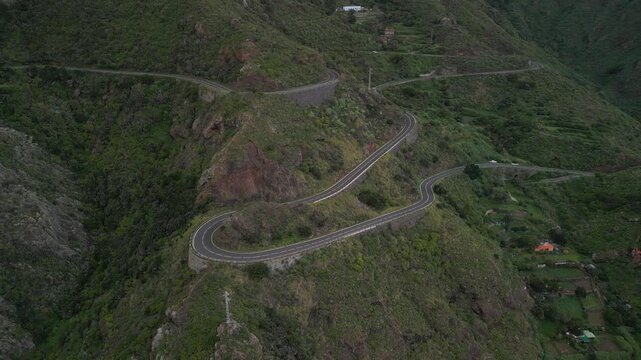 A winding road carves through a lush green mountainous landscape with houses nestled on the slopes.