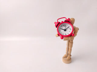Small, red, retro-style analog alarm clock held by a wooden articulated mannequin
