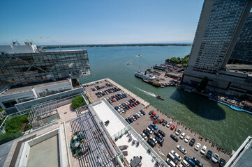 Obraz premium Toronto's busy waterfront features modern architecture, a parking lot, marina with various boats, and the vast expanse of lake ontario under a clear blue sky