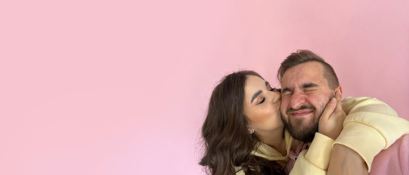 Mobile photo banner. Young adult woman in yellow sweatshirt hugs and kisses mature man with beard and closed eyes in pink hoodie on cheek. Concept of love, 14 february, Valentine day. Copy space