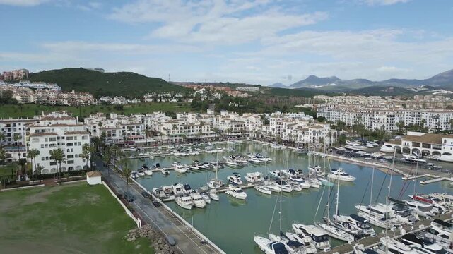 Drone footage showing Puerto de la Duquesa in Manilva, featuring boats, waterfront apartments, hills and the Mediterranean coastline.
