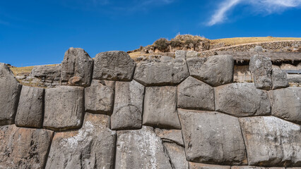 Ruins of an ancient Inca fortress Sacsayhuaman. A wall of huge boulders, sanded and closely fitted. Ashlar polygonal masonry. Yellowed grass on the hillside. Blue sky, clouds. Peru. Cusco.