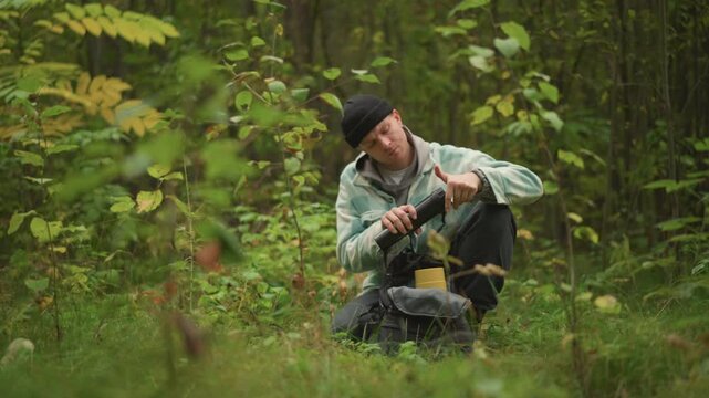 caucasian hiker sitting in forest checking compass and map while crouched among mossy undergrowth acts as navigator, scout and survivalist inspecting gear, adjusting backpack and peering into
