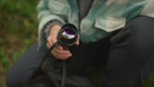 white explorer extends green spotting tube, inspects lens element and then packs scope and thermos into backpack organized field teardown, gear check, pockets and zippers, quiet trail rest