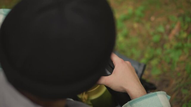 Caucasian hiker preparing scope from backpack, topdown shots show hands removing padded case and extending beige optical tube, twisting eyepiece cap and securing components, wearing knit beanie