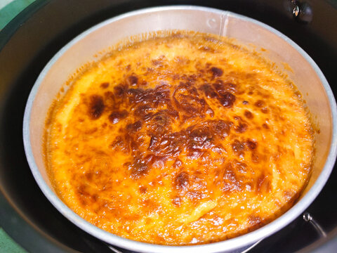 Top view of a baked custard with a deeply caramelized surface, cooked in a metal pan. The image emphasizes warmth, texture, and the handcrafted feel of oven-made desserts