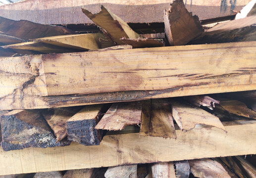 Close-up of stacked rough wooden planks showing raw natural texture, saw marks, bark edges, and rugged lumber surface used for carpentry, woodworking, and construction material supply