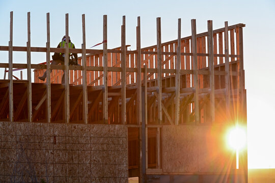 Construction worker on a framed commercial building at sunrise, representing structural assembly, exterior building progress, and early morning jobsite activity