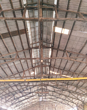 Symmetrical view of an old industrial warehouse roof with metal sheets, wooden beams, rustic textures, and strong architectural industrial structure