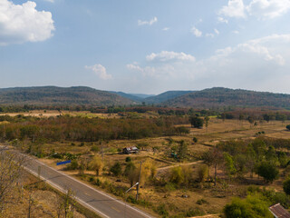 High-angle drone photography of Wang Thong village, a small rural settlement nestled in the Phu Phan Mountains, Thailand, showcasing colorful autumn foliage and peaceful countryside landscape.