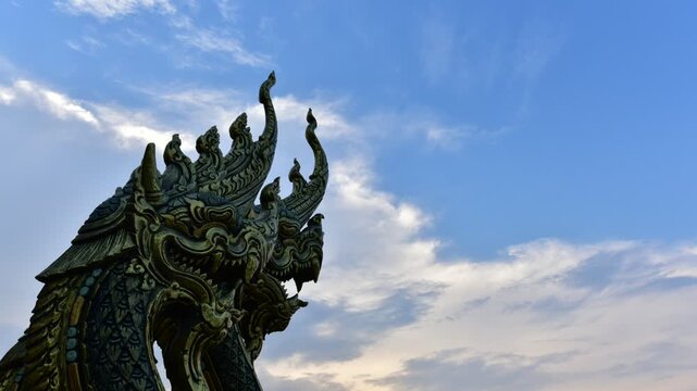 Naga serpent statue with a backdrop of a temple under a bright blue 