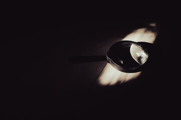 Magnifying glass lying on a dark surface with dramatic light beam, concept of discovery, investigation, hidden truth and research in the dark.