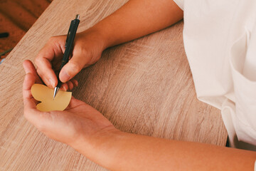Person hand writing or drawing on paper heart on wooden table background, concept of romantic message, mental health care, and kindness.