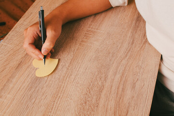 Person hand writing or drawing on paper heart on wooden table background, concept of romantic message, mental health care, and kindness.