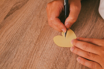Person hand writing or drawing on paper heart on wooden table background, concept of romantic message, mental health care, and kindness.