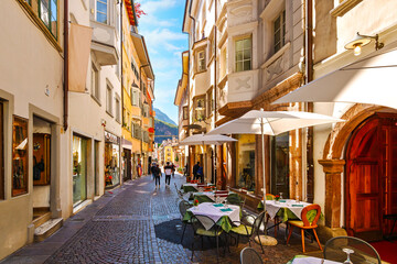 Obraz premium A narrow cobblestone pedestrian street with shops and sidewalk cafes in the historic old town center of Bolzano, Italy, in the South Tyrol province of Northern Italy.