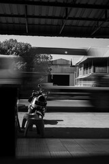 Black and white photo of a vintage model scooter parked on the roadside, capturing motion blur of passing vehicles and urban street atmosphere