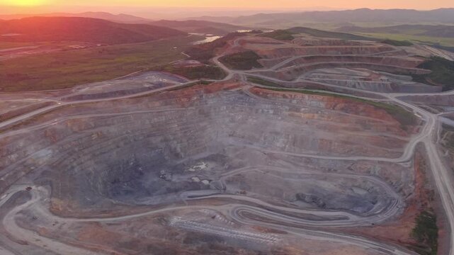 Aerial view of open pit mine at sunset with expansive landscape and dramatic sky, gold ore industry.