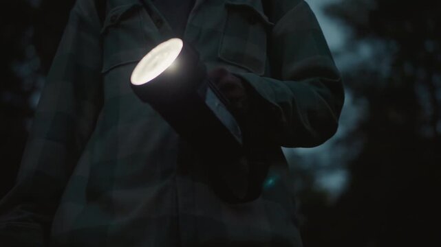 flashlight beam sweeping dark forest, white hiker scouting trail with large torch, plaid shirt and backpack strap visible, dusk sky through pines, tense quiet atmosphere and focused movement