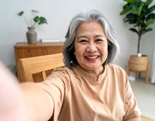 Smiling older woman with silver hair takes a selfie indoors, framed by chair and indoor plants background