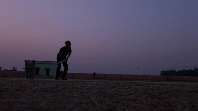 Silhouette of a unrecognized batsman standing near the pitch during calm sunset light.
