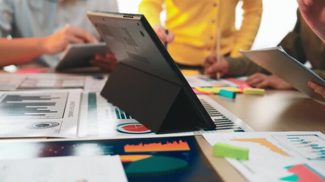 A diverse group of professionals engaged in a collaborative meeting, analyzing business reports and discussing strategies for improvement in a modern office environment. SACTR