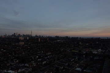 Naklejka premium Toronto cityscape showcasing iconic skyscrapers and a vast urban core blending into a residential neighborhood at twilight, with the lake visible on the horizon