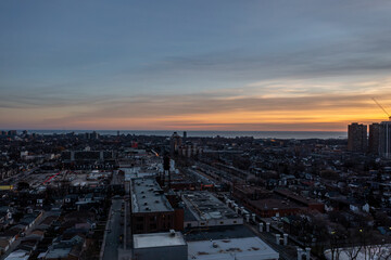 Naklejka premium Toronto skyline with residential and industrial buildings stretching along lake ontario, bathed in warm golden hour light as dusk paints the sky orange and blue over the cityscape