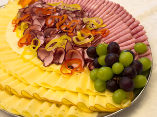 Close up of meat and cheese platter with sliced ham, smoked meat, cheese, grapes and vegetables. Catering food arrangement suitable for buffet, celebration or event.