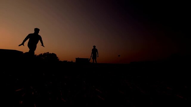 Silhouette of a unrecognized cricket player practicing at sunset against a dramatic evening sky.