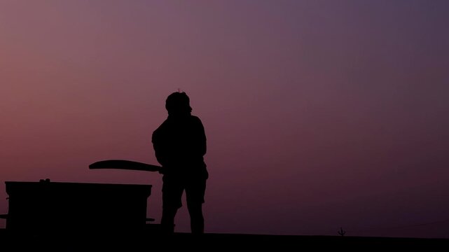 Unrecognized cricket player silhouette standing with bat during evening golden hour. Clean sports background footage for cricket reels, tournament visuals, promotional videos, and broadcast design.