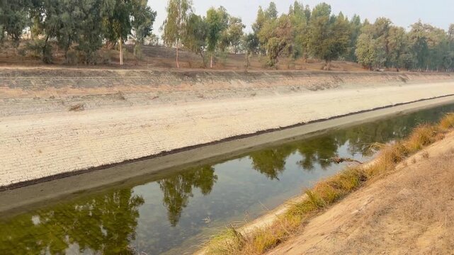 Wide cinematic side-view video of a brick-lined rural canal running through a forest, both canal walls visible with bricks forming clean, parallel edges