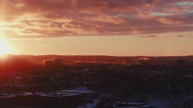 Dramatic sunset over a small town. The warm golden light washes over the niagara escarpment and lights up the vapour pouring from the rooftops of buildings on a cold snowy night.