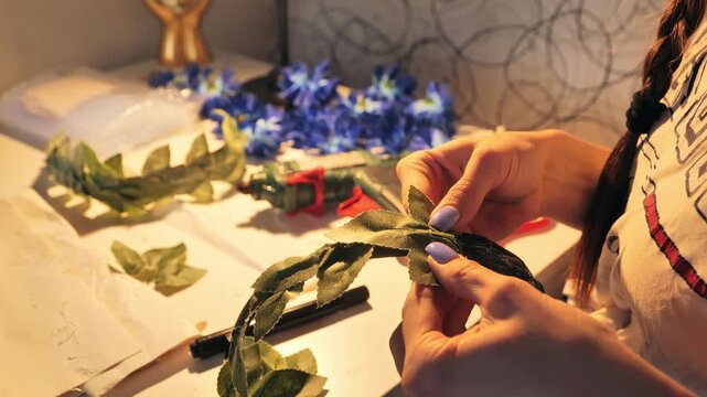 Hands assembling artificial leaves into decorative flower wreath on craft table