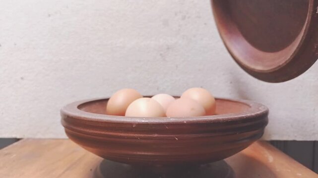 Hand placing a fresh brown egg on top of a pile in a clay bowl