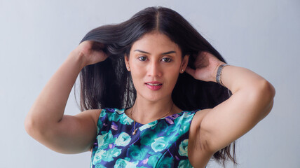 Fototapeta premium A beautiful woman with long, black hair is showing off her beautiful locks by tossing them aside. She's wearing a sleeveless, blue, floral-patterned dress, exposing her armpits.