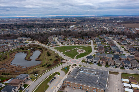 Aerial view showing a modern residential community in brampton, ontario, canada, with houses, streets, a park, a retention pond, and a school building harnessing solar energy