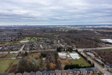 Naklejka premium Suburban neighborhood in brampton, ontario with residential houses, a golf course, greenhouses, roads, and a visible toronto city skyline under an overcast sky
