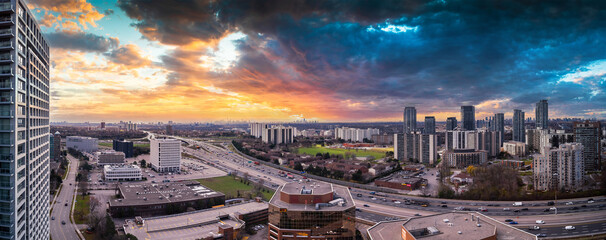 Naklejka premium Toronto cityscape showing urban development with multiple high rise buildings and busy highway traffic flowing under a dramatic, colorful sunset sky with dark clouds