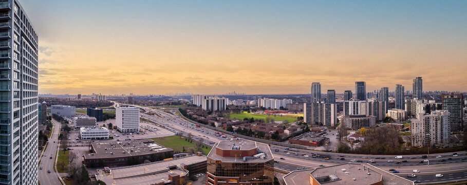 Mississauga city panorama showcasing modern skyscrapers, residential buildings, and the busy highway with car traffic flowing during a golden hour twilight