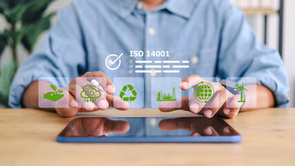 ISO 14001 environmental management system concept. Business professional using digital tablet with sustainability, recycling, CO2 reduction, and renewable energy icons. © phimprapha