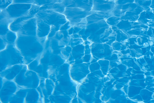 Blue water surface texture with bright sun ripples,caustics effect in swimming pool.Clear blue swimming pool water with sunlight reflection,wave.Background for summer,travel,spa,relaxation,tropical