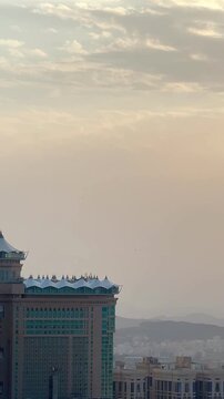 A stunning cinematic shot of the modern Jabal Omar complex architecture with its iconic skybridge, overlooking the city of Makkah, Saudi Arabia, during a hazy golden hour with dramatic sunlight.