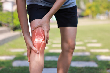 Close-up of hand holding painful injured knee with red inflamed spot and X-ray bone skeleton joint overlay. Medical concept of fracture, arthritis, tendonitis, or muscle ache in outdoor background.