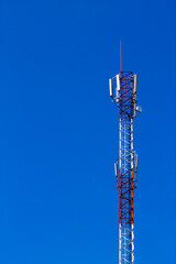 Red and white telecommunication tower with antennas for mobile communication against clear blue sky.